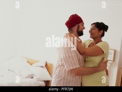Man and pregnant woman hugging each other, both smiling Stock Photo