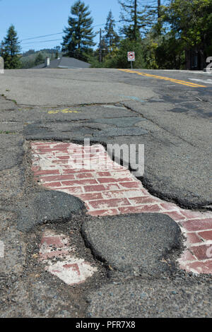 Asphalt wears away to reveal the history of a street constructed of brick . Stock Photo