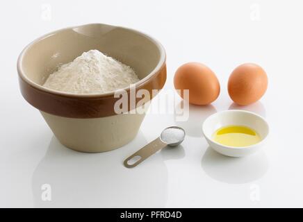 Cooking ingredients, bowl of flour, olive oil, salt in measuring spoon, and two eggs Stock Photo