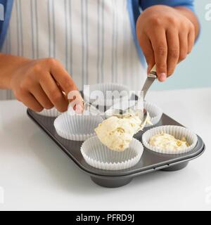 Boy's hands spooning vanilla cake mixture into paper cases in a muffin tray Stock Photo