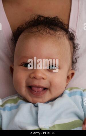 Head and shoulders of smiling baby boy, held by a woman, close-up Stock Photo