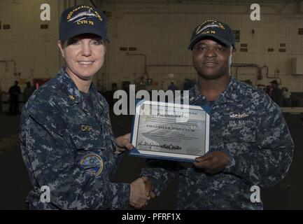 NORFOLK, Va. (May 24, 2018) -- Personnel Specialist 2nd Class Igbekele Oki, from Nigeria, assigned to USS Gerald R. Ford's (CVN 78) administration department, receives his enlisted surface warfare specialist certificate from Lt. Cmdr. Melissa Chope, Ford's administration officer, during an awards ceremony in the ship's hangar bay. Stock Photo