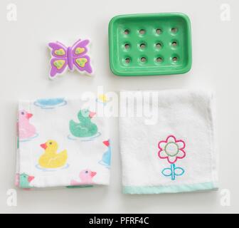 Butterfly shape soap, green plastic soap dish and two folded flannels decorated with ducks and flower Stock Photo