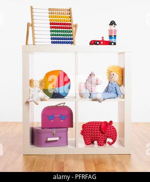 Various toys in bookcase, including suitcases, stuffed toys, ball, abacus Stock Photo