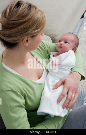 Three week old baby looking up at her mother who is cradling her in her arms Stock Photo