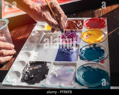 Hand of artist blending acrylic color by paintbrush in artist palette on wooden table background for working in art studio. Stock Photo