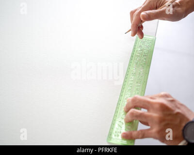 Hands hold the wooden pencil with green ruler on blank white canvas with copy space. Stock Photo