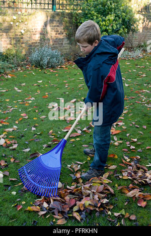 Child and rake in autumn garden. Kid raking leaves in fall. Gardening ...