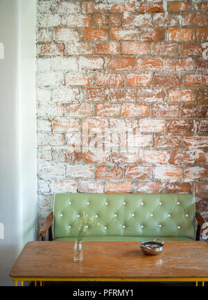 Loft Interior Cafe with Green Vintage Leather Sofa, Flower in Clear Vase Bottle and Stainless Bowl on Wooden Coffee Table on Grunge Brick Wall Backgro Stock Photo