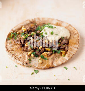 Flatbread topped with finely chopped lamb, toasted pine nuts and hummus, and garnished with fresh mint leaves Stock Photo