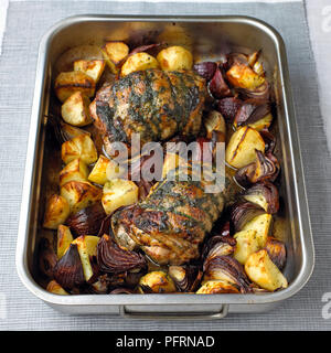 Lamb with red onions and roast potatoes in stainless steel roasting pan on grey tablecloth Stock Photo