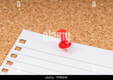 Piece of lined paper and red push pin attached to cork pin board, close-up Stock Photo