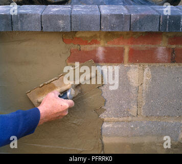 Man using trowel to render inside wall of sunken concrete pond with fibre-reinforced concrete Stock Photo