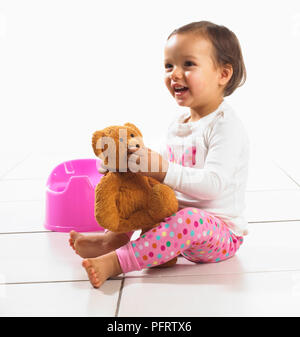 Toddler girl holding soft toy, potty in background, 1.5 years Stock Photo