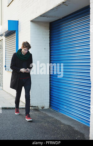 Young man walking down street looking at mobile phone Stock Photo