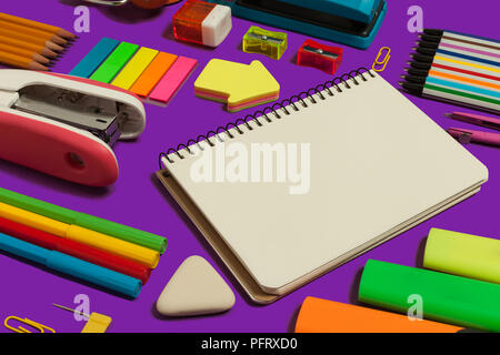 colored various stationary surrounding an opened notebook lying on a purple background. concept of office and educational chancery Stock Photo
