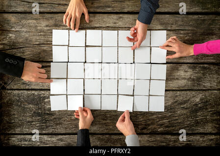 Top view of six hands, male and female, assembling a collage of blank white cards over textured wooden rustic boards. Stock Photo