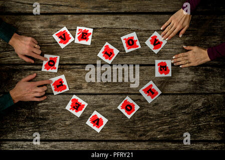 Top view of male and female hands holding a Love sign spelled on individual cards placed in a heard shape over rustic textured wooden desk. Stock Photo