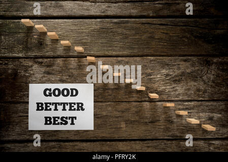Top view of Good Better Best message written on white paper card laying  next to a steps made of wooden pegs resembling a staircase with textured oak  Stock Photo