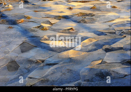 Fractured pieces of ice on the banks of the River Dee at Kirkcudbright, Scotland. Early morning winter sunshine picks out random fragments and creates a cubism pattern Stock Photo