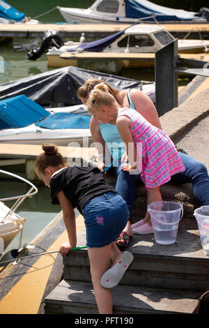 UK, Cornwall, Padstow, The Strand, young girls fishing for crabs from Quayside steps with mother Stock Photo