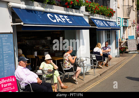 UK, Cornwall, Padstow, The Strand, visitors sat in sunshine outside waterfront Fish and Chip shop Stock Photo