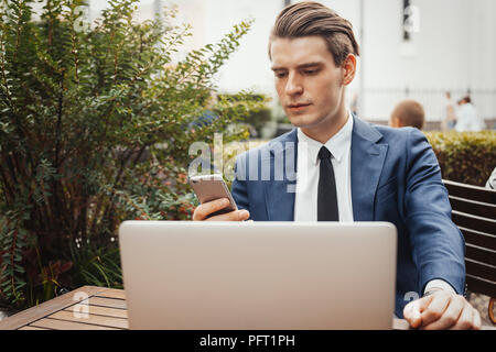 Business man holding mobile phone in hand and sitting next to laptop. Front view Stock Photo