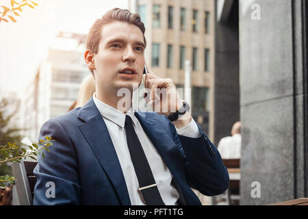 Young brunette businessman talking by mobile phone and looking straight. Stock Photo