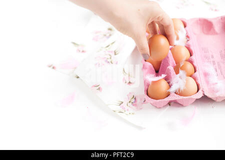 Pink Box with chicken eggs. PEARA and a towel with flowers for decoration. Eggs on white background and hand in frame. FOR Easter. Top view Stock Photo