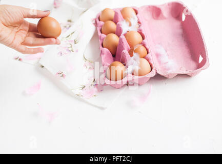Pink Box with chicken eggs. PEARA and a towel with flowers for decoration. Eggs on white background and hand in frame. FOR Easter. Top view Stock Photo