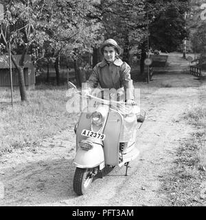 Rain in the 1950s. A young woman wearing raincoat is driving her scooter NSU Prima. Sweden September 1959 Stock Photo