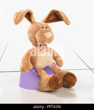 Toy rabbit sitting on purple potty Stock Photo