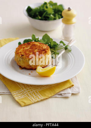 Fishcake cut in half on plate, served with cress garnish and lemon wedge Stock Photo