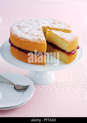 Victoria sandwich cake filled with jam and dusted with icing sugar, sliced Stock Photo
