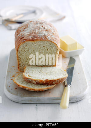 Farmhouse loaf with some slices cut away, bread knife and butter nearby Stock Photo
