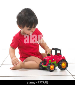 Baby boy (16 months) sitting with toy tractor Stock Photo