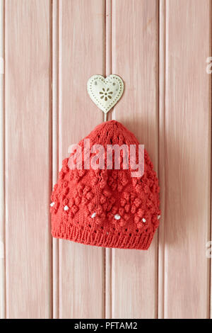 Red knitted beanie hat hanging on hook Stock Photo