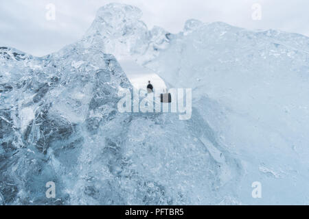 Looking through the hole in an iceberg gives a unique view of tourists on Diamond Beach in Iceland. Stock Photo