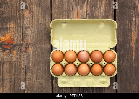 eggs in a cardboard box on a wooden table,  shot directly above, copy space Stock Photo