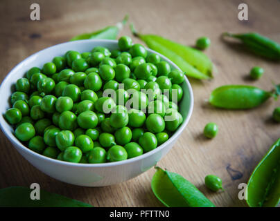 A bowlful of fresh, organic garden peas that have been freshly picked and removed from their pods on a rustic wooden table top. Stock Photo