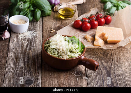 Vegetarian pesto pasta with cheese in bowl and Italian food ingredients on rural wooden table Stock Photo