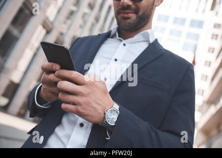Confident businessman. Businessman on city street checking time and using smart phone. Focus is on hands Stock Photo