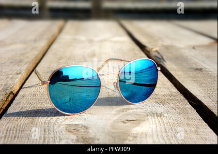 fashionable mirror glasses with blue glasses on the sun lie on a wooden floor rest trip reflected in glasses Stock Photo