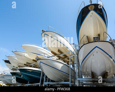 View from below of the hulls of motorboats racked one above another on two levels in a dry rack boat storage facility against blue sky. Stock Photo