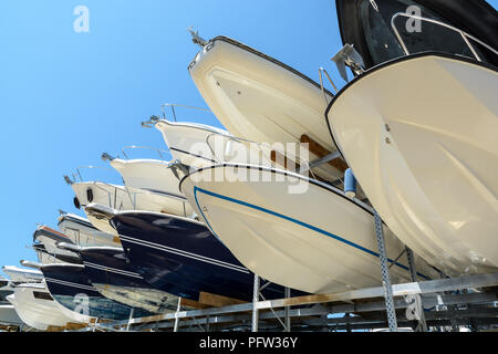 View from below of the hulls of motorboats racked one above another on two levels in a dry rack boat storage facility against blue sky. Stock Photo