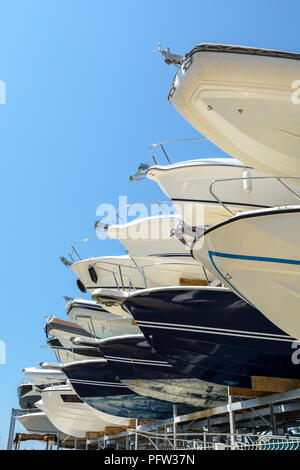 View from below of the hulls of motorboats racked one above another on two levels in a dry rack boat storage facility against blue sky. Stock Photo