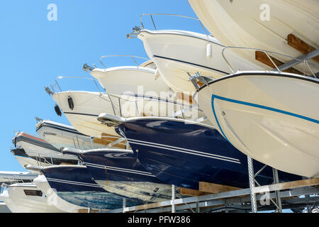 View from below of the hulls of motorboats racked one above another on two levels in a dry rack boat storage facility against blue sky. Stock Photo