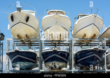 View from below of the hulls of motorboats racked one above another on two levels in a dry rack boat storage facility against blue sky. Stock Photo