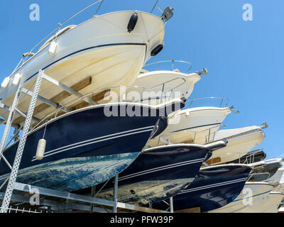 View from below of the hulls of motorboats racked one above another on two levels in a dry rack boat storage facility against blue sky. Stock Photo