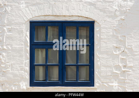 Blue painted wooden window frame set in whitewashed brick and stone wall. Stock Photo